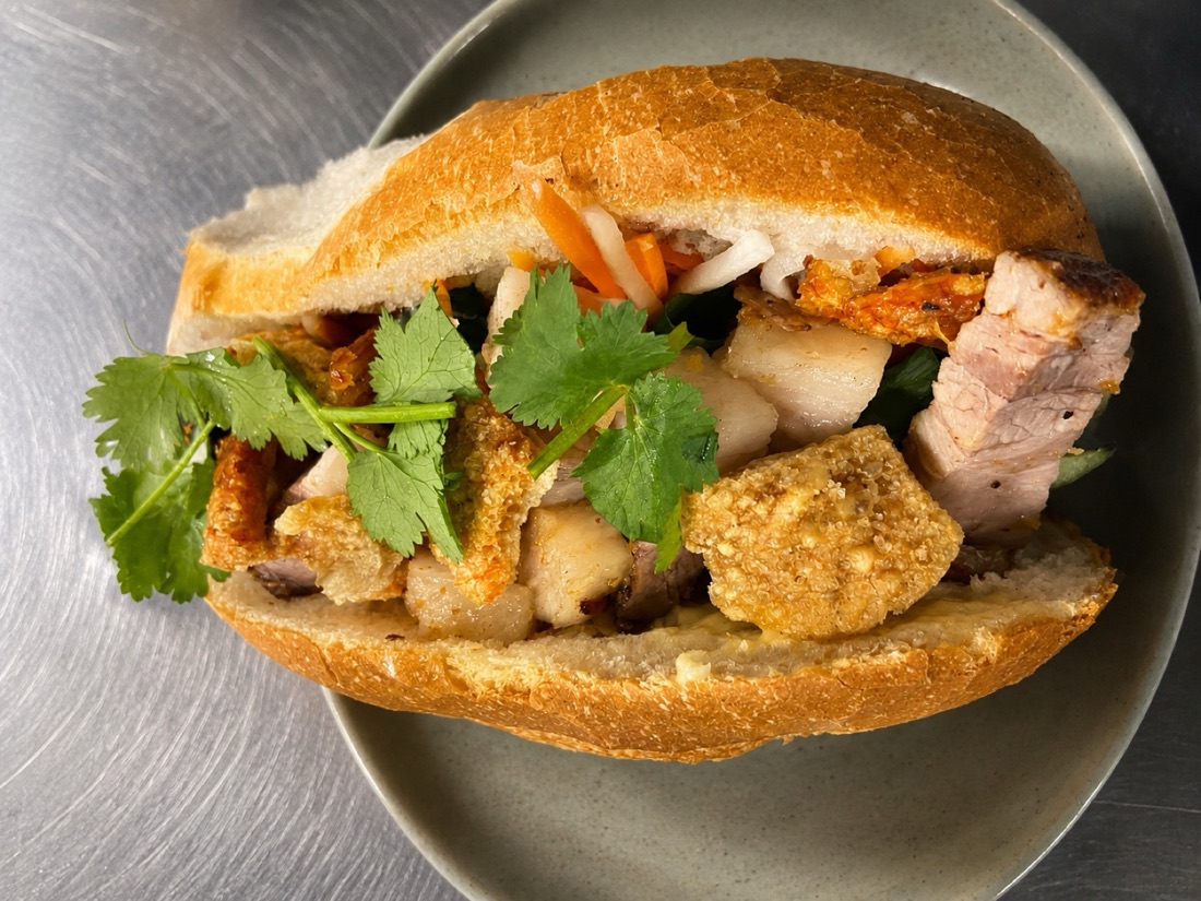 Close-up of a roast pork bánh mì at Asian Tucker in Tanunda, with crackling, pickled carrot and fresh coriander in a crusty roll