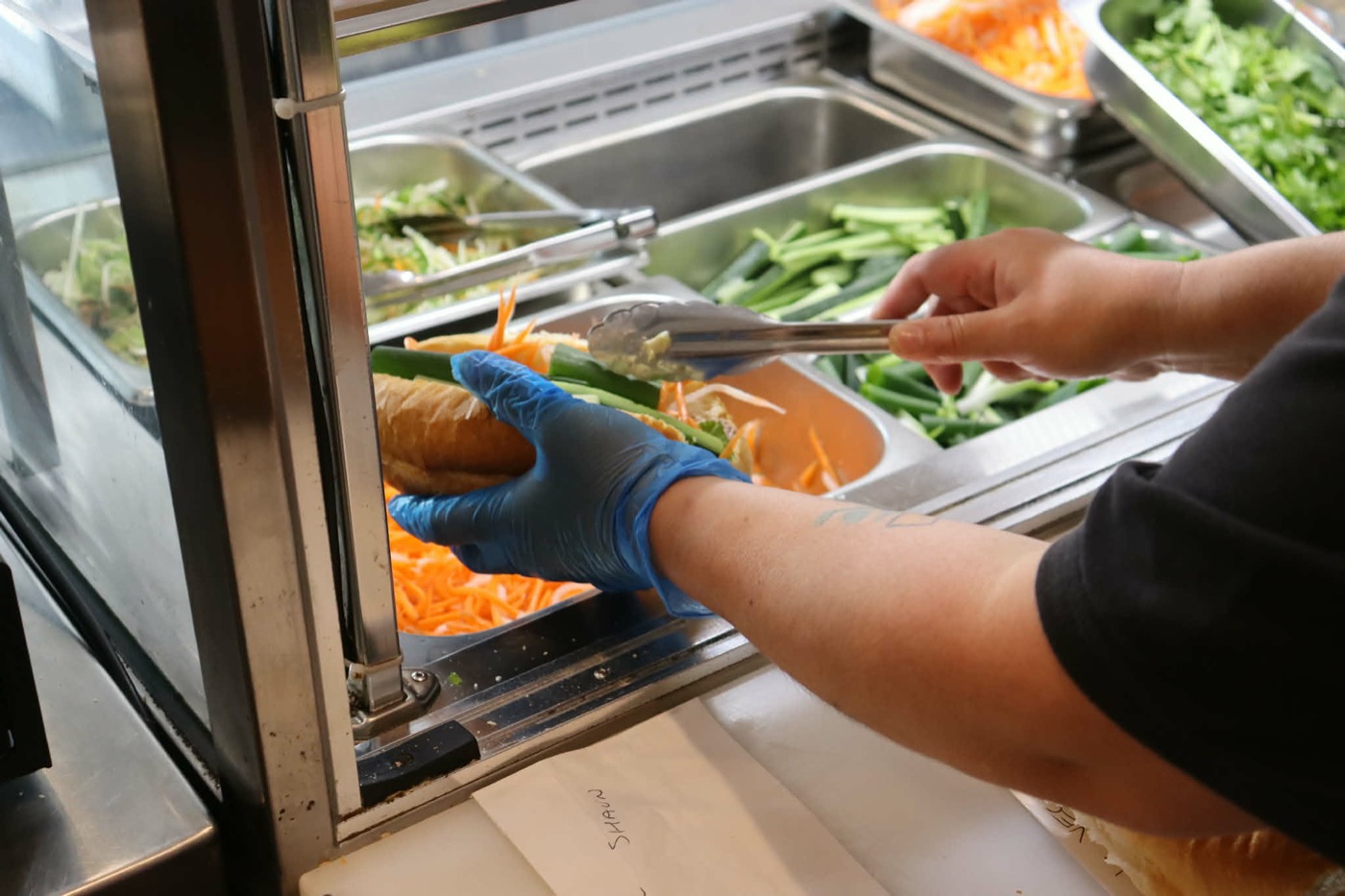 A bánh mì being filled at the salad bar