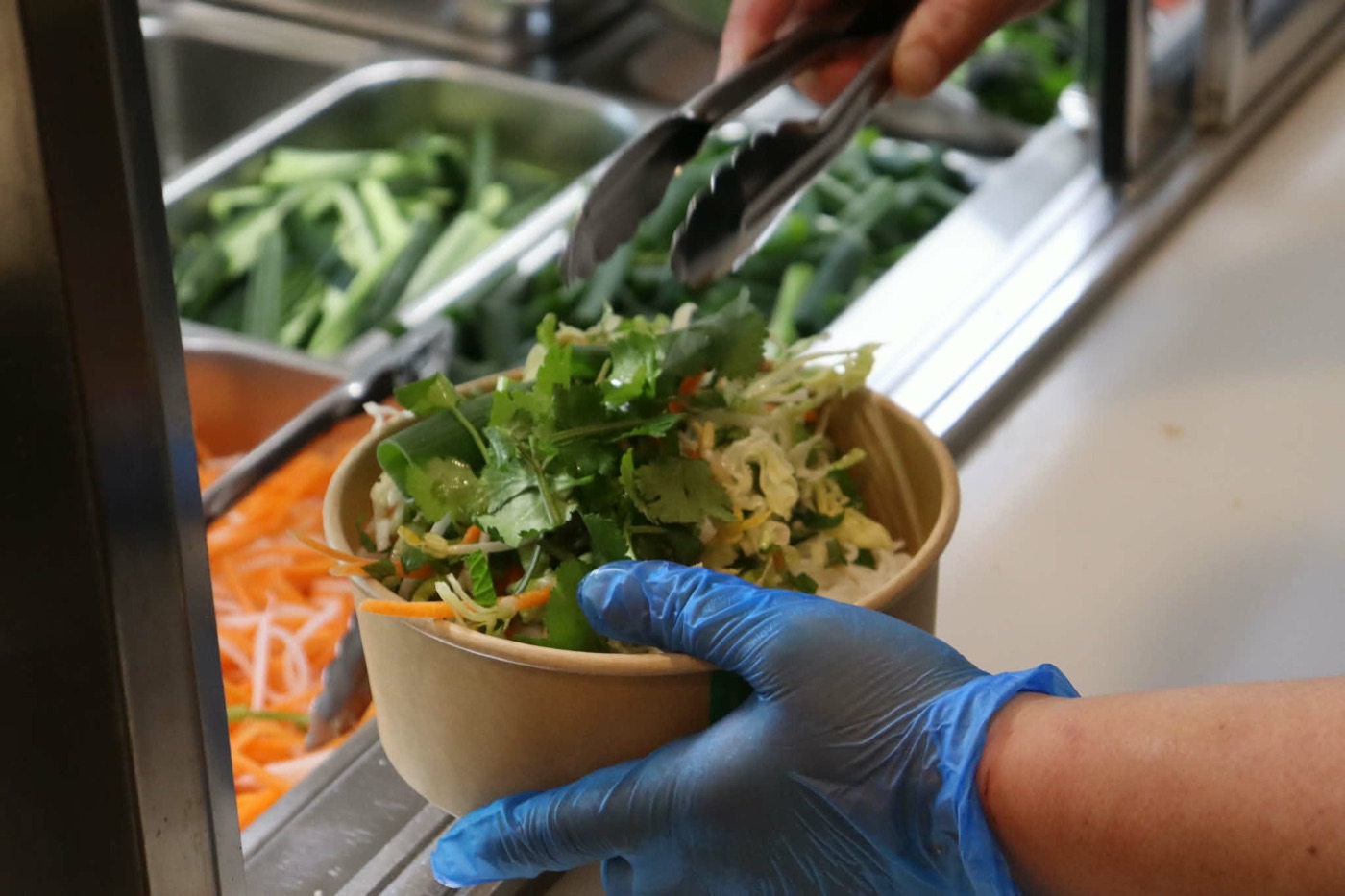 A salad bowl being topped with fresh coriander at the counter