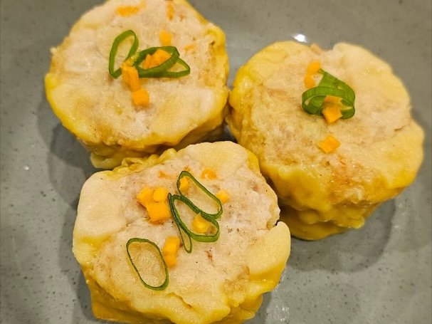 Three steamed pork dimmies topped with spring onion and diced carrot on a grey plate at Asian Tucker, Tanunda