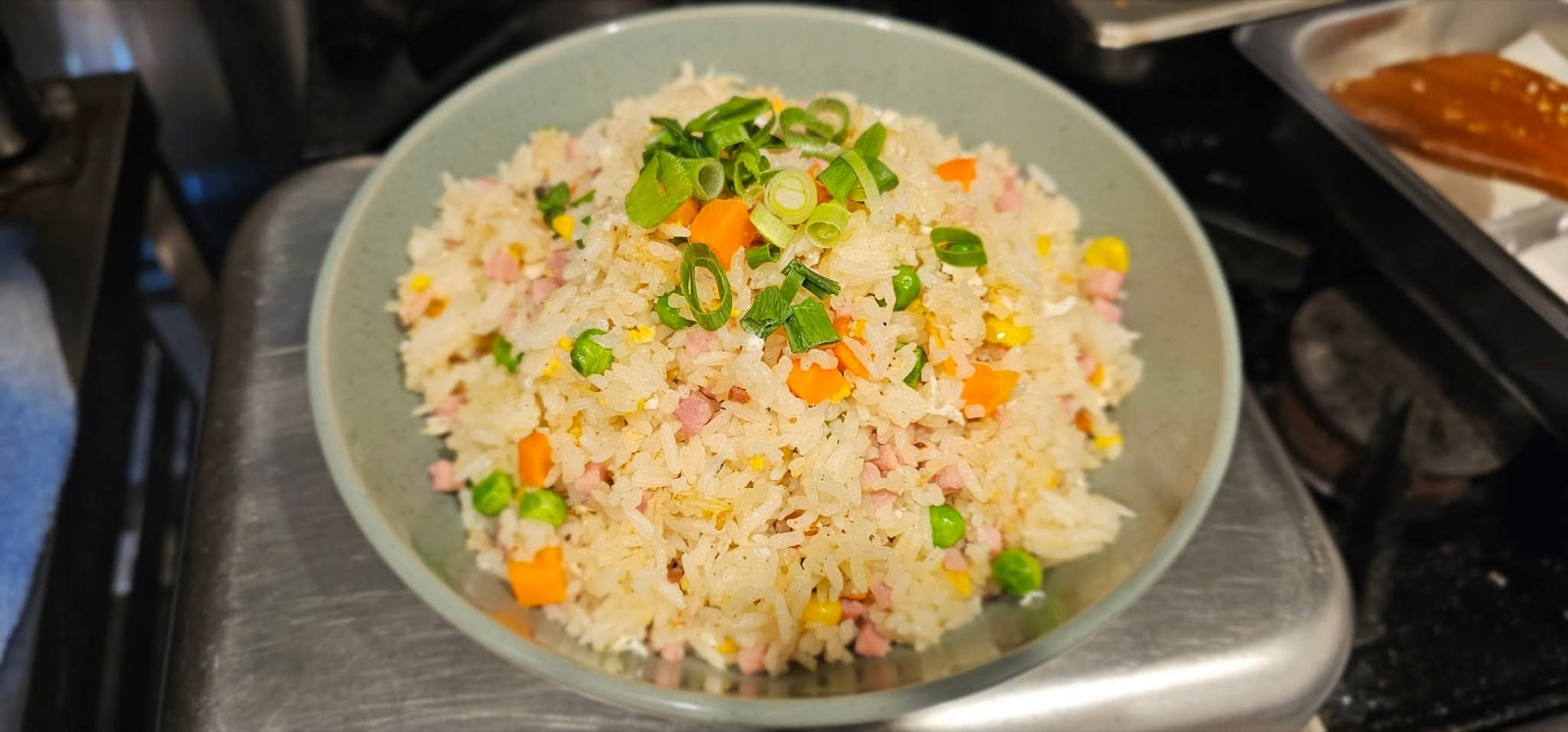A heaped bowl of fried rice with egg, peas and spring onion