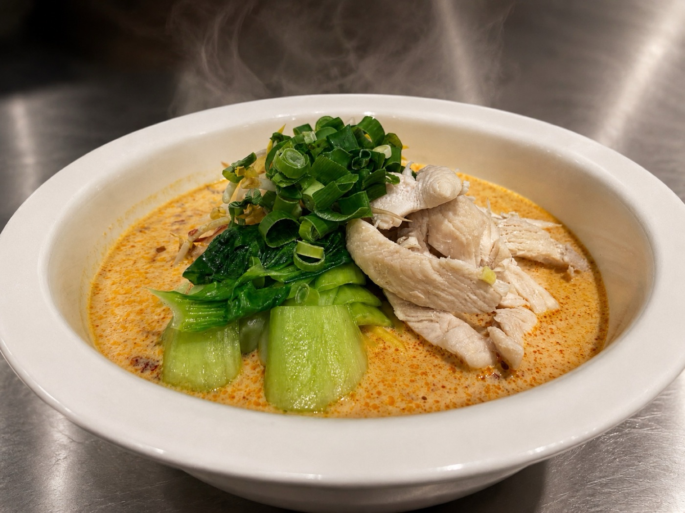 A bowl of chicken laksa at Asian Tucker in Tanunda, with sliced chicken, greens and spring onion in a golden coconut broth