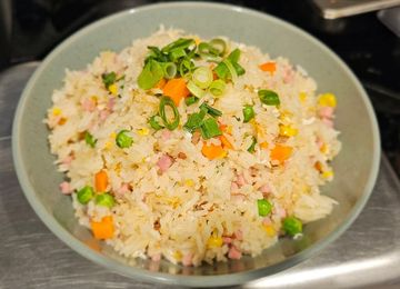 A bowl of fried rice with peas, carrot and spring onion