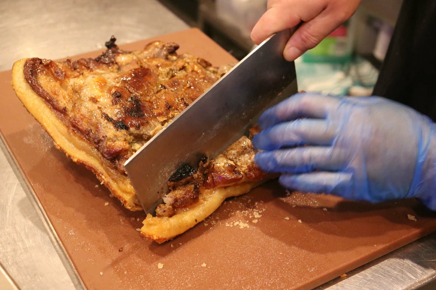 A cleaver going through crispy roast pork on the chopping board